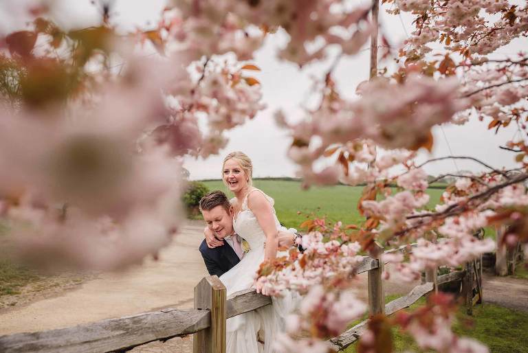Groom lifts the bride in amongst the cherry blossom at their Bartholomew Barn wedding