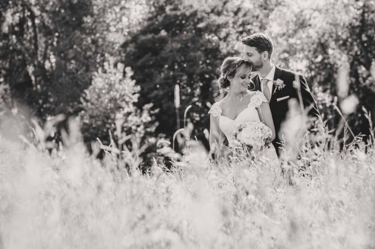 black and white photo of groom kissing bride on the head in the Grittenham Barn meadow